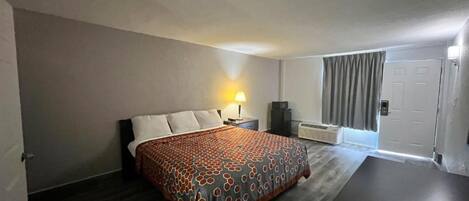 Habitación de hotel con cama, mesita de noche, lámpara y vistas al exterior.
