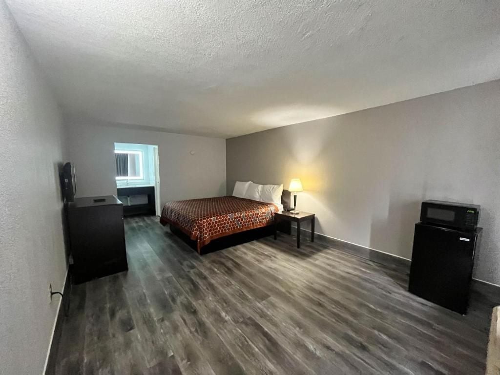 A hotel room with a bed, bedside table, lamp, and a small black appliance, possibly a microwave.