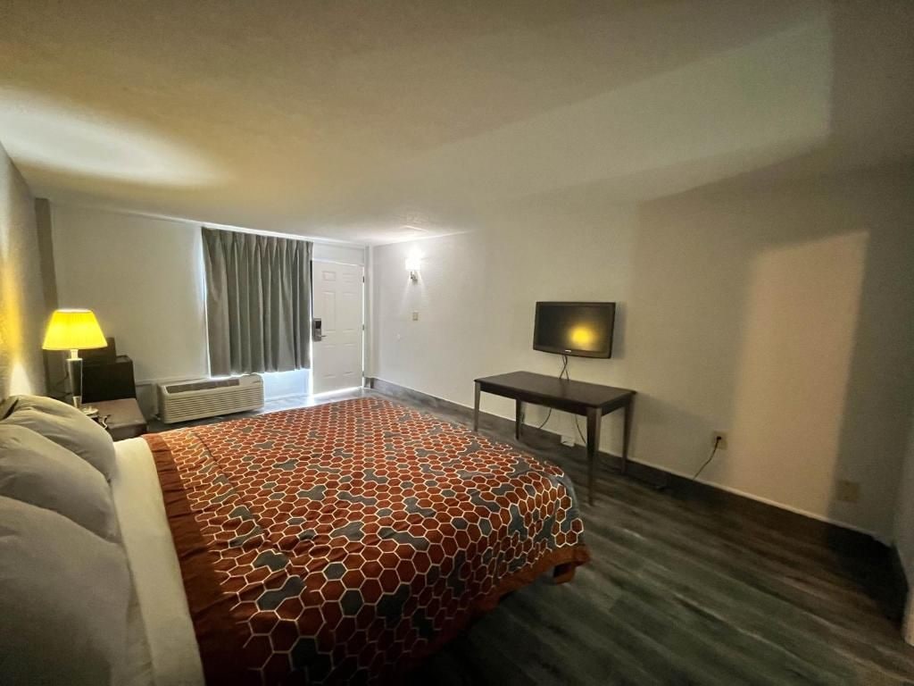 Una habitación de hotel con una cama grande, un televisor sobre un mueble bajo, un escritorio y una ventana con cortinas.