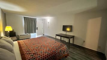 Una habitación de hotel con una cama grande, un televisor sobre un mueble bajo, un escritorio y una ventana con cortinas.