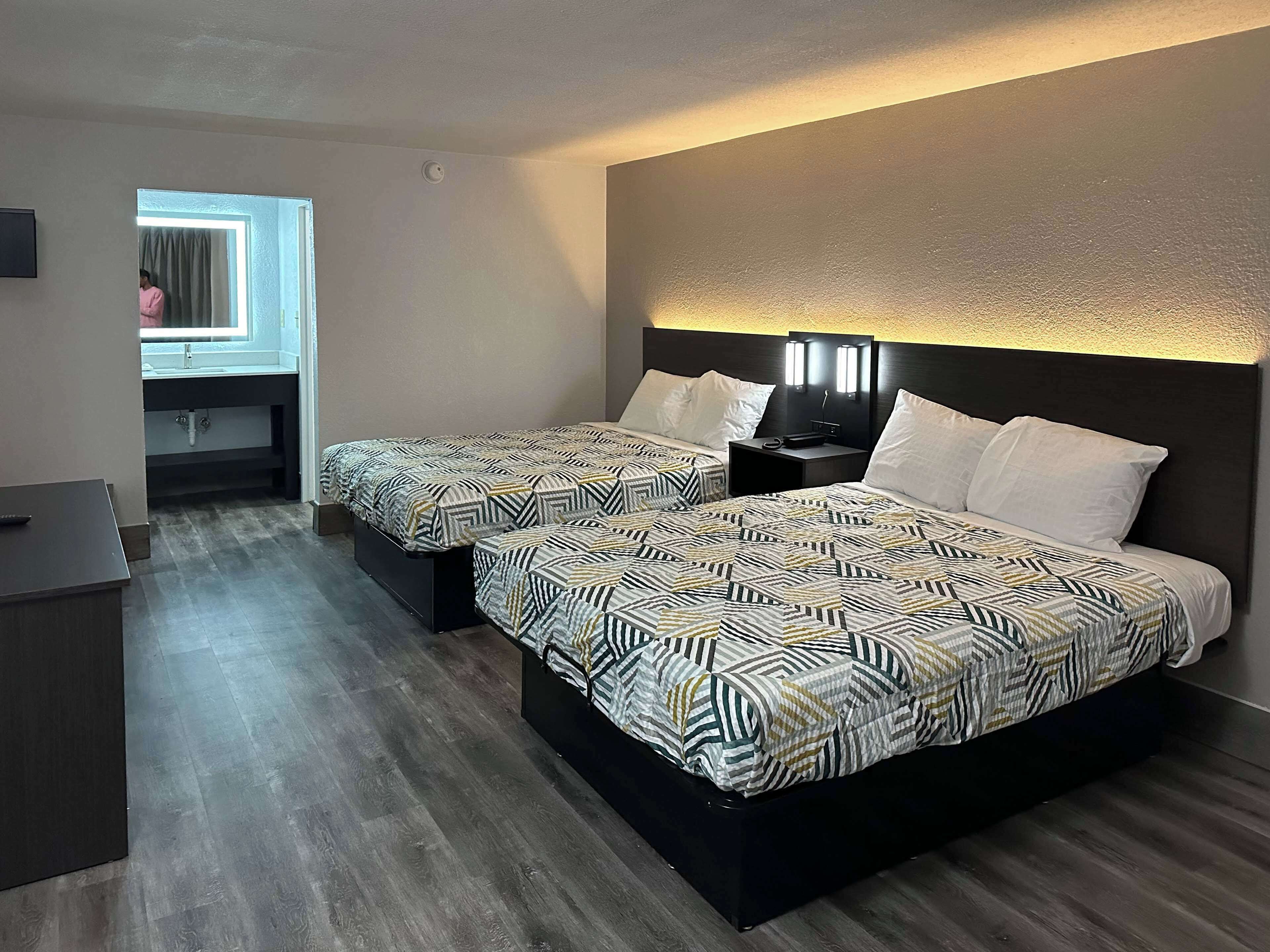 Een hotelkamer met twee bedden, een bureau, een raam met gordijnen en een wandlamp.