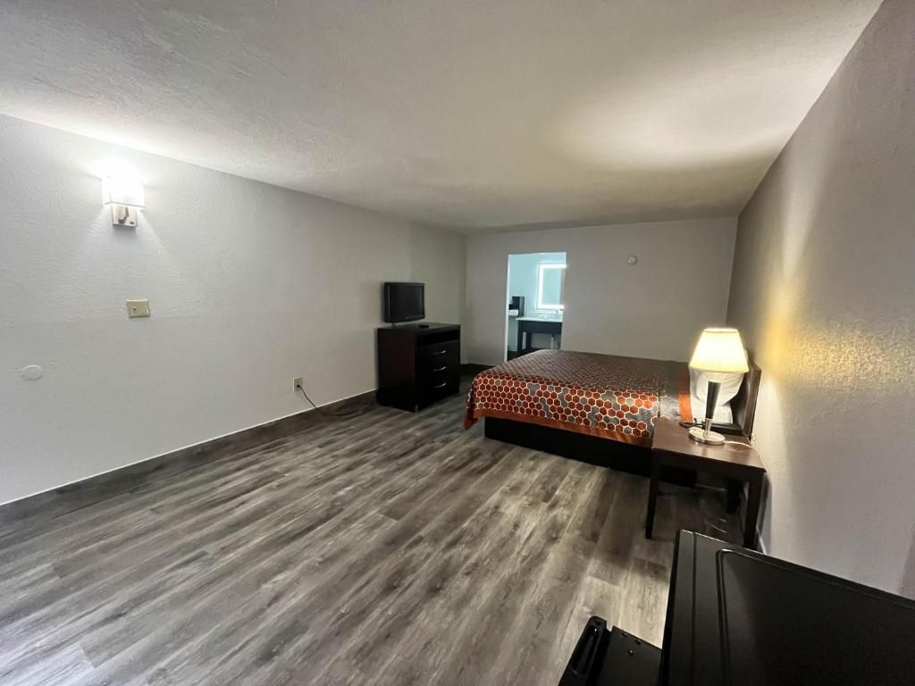 Un dormitorio con cama, escritorio, lámpara, televisor y cómoda.