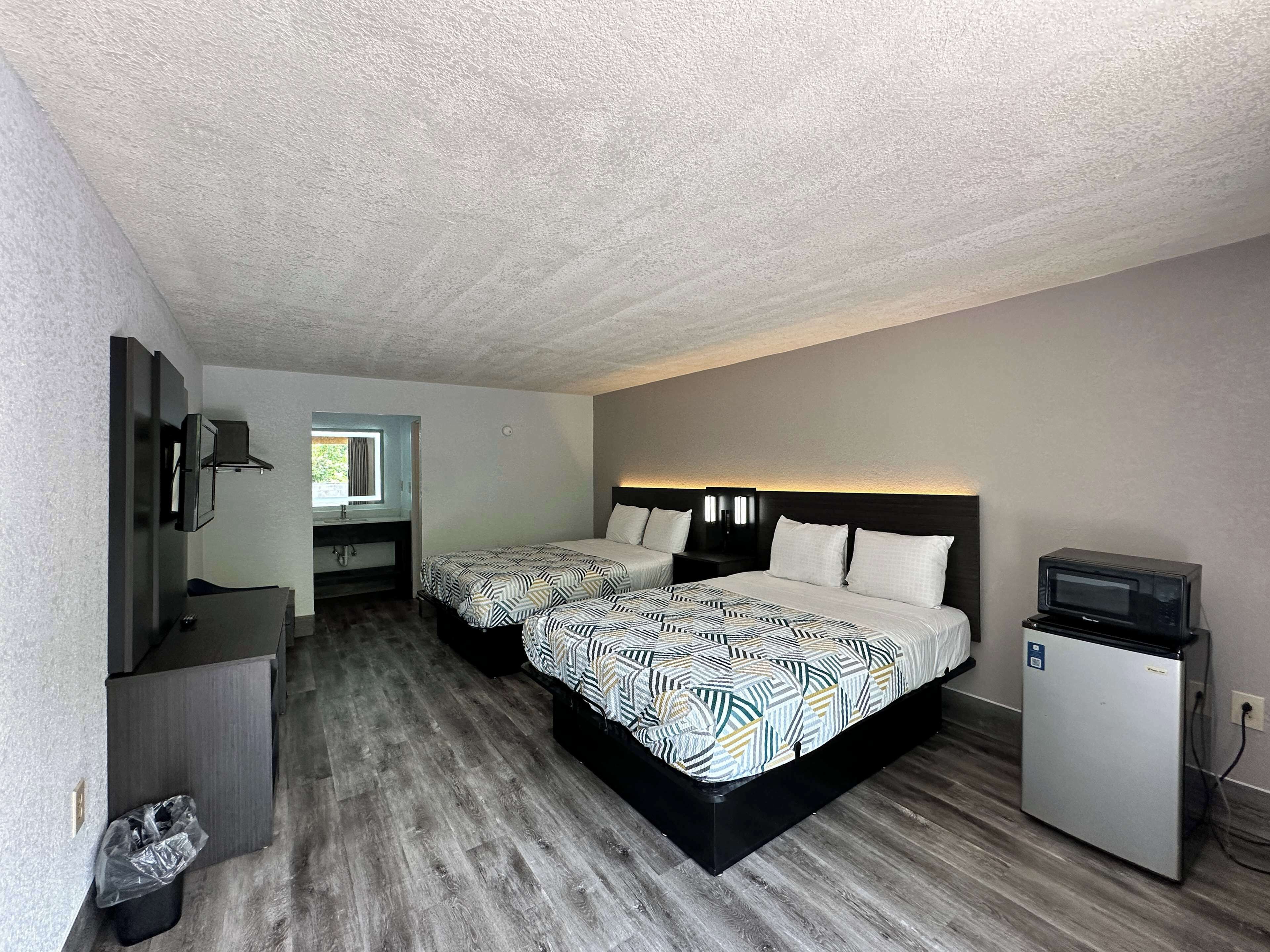 A hotel room with two beds, a small desk, a TV, and a refrigerator.