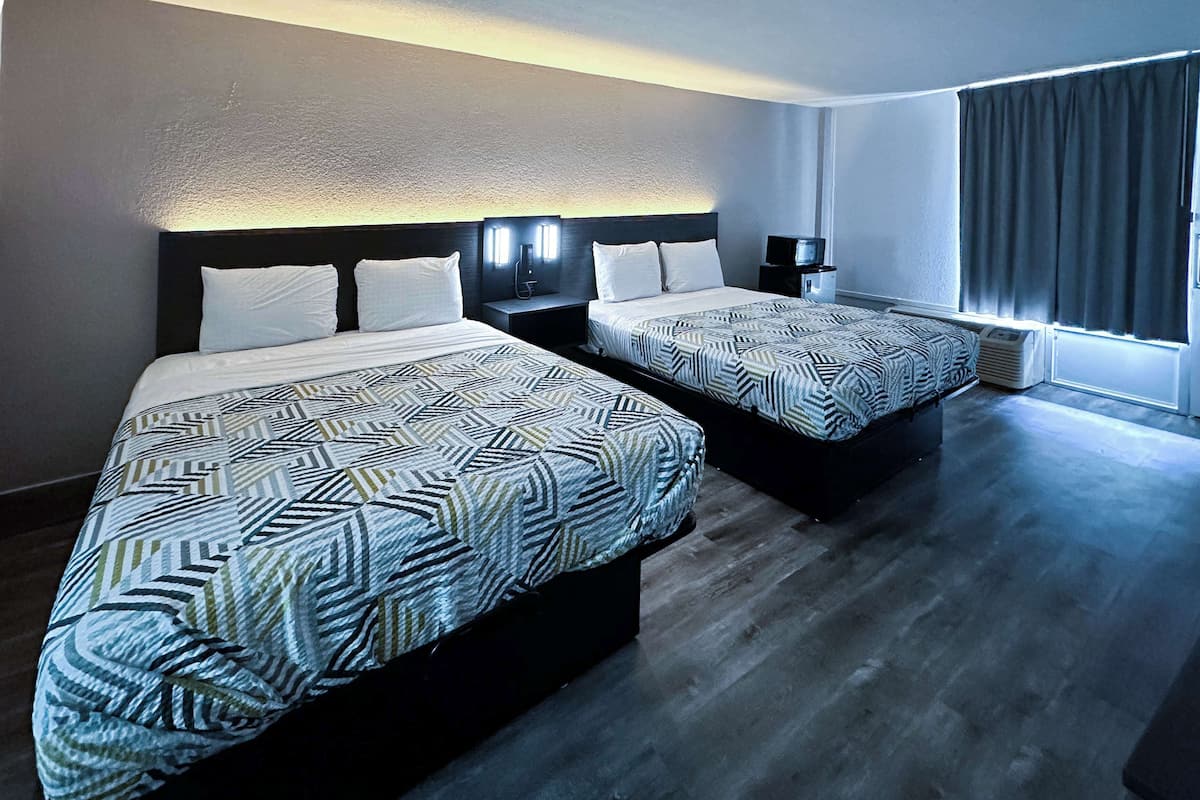 Een hotelkamer met twee bedden, elk voorzien van beddengoed met een patroon, een nachtkastje met een televisie en een raam met gordijnen.