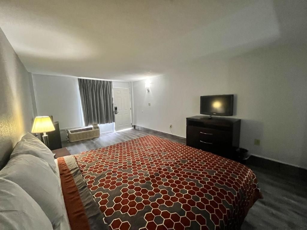 Habitación de hotel con cama, televisor de pantalla plana, cómoda y ventana con cortinas.