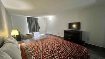 Habitación de hotel con cama, televisor de pantalla plana, cómoda y ventana con cortinas.