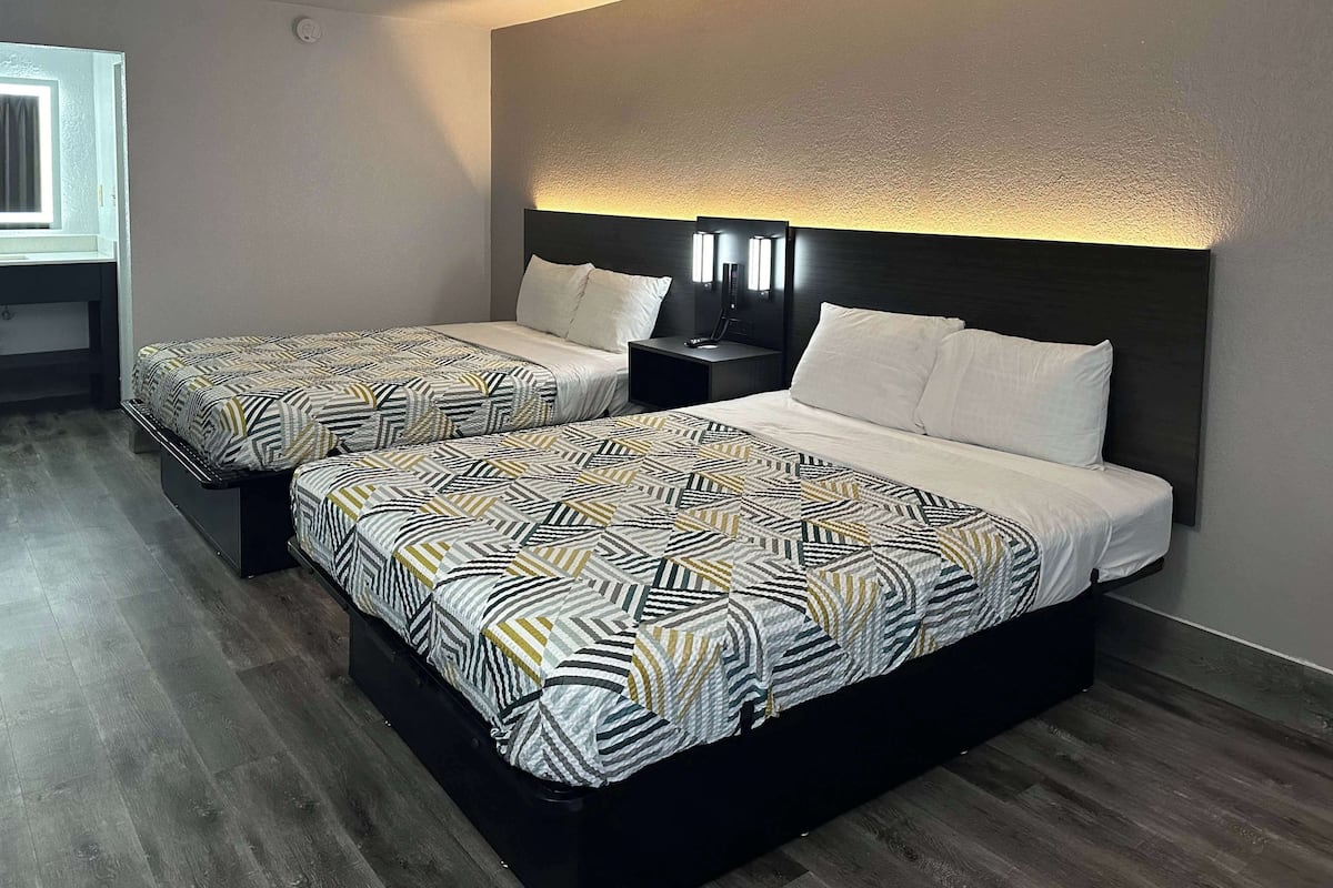 Een hotelkamer met twee bedden, elk voorzien van beddengoed met een patroon, een donker hoofdeinde, nachtlampjes en een klein tafeltje.