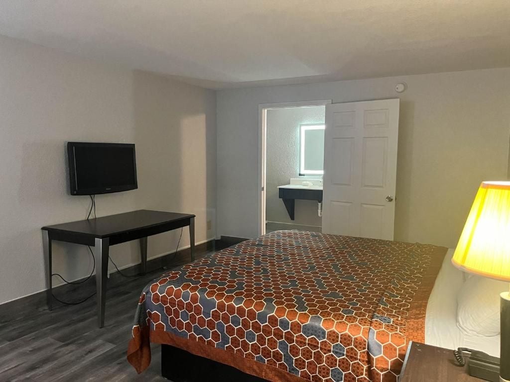 A hotel room with a bed, a desk, a television, and a lamp.