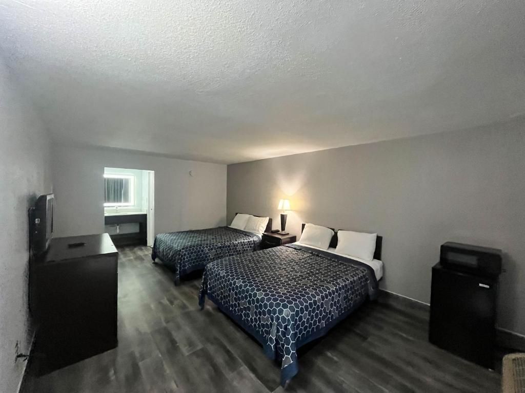 A room with two beds, a desk, a lamp, and a trash bin.