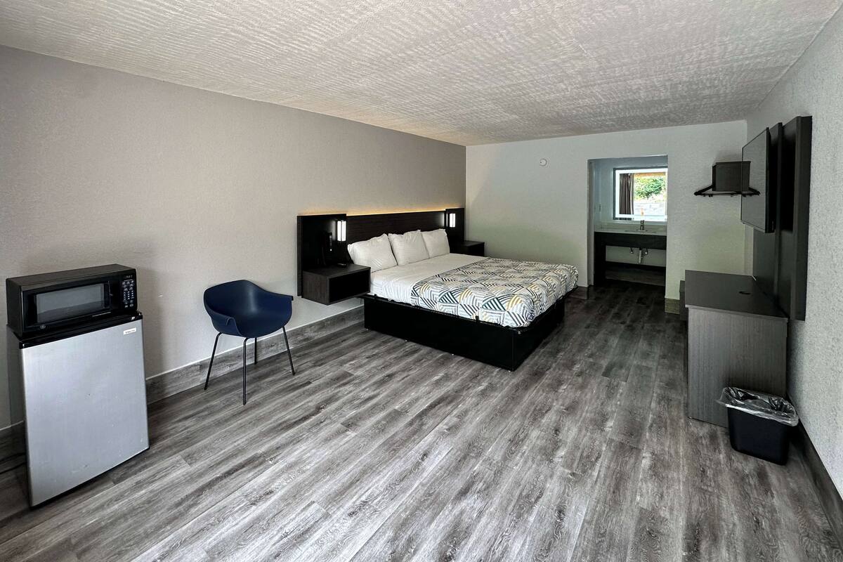 Een kleine hotelkamer met een bed, een bureau met stoel, een magnetron en een kleine prullenbak.