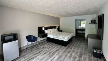 Una habitación de hotel pequeña con cama, un escritorio con silla, un microondas y un cubo de basura.