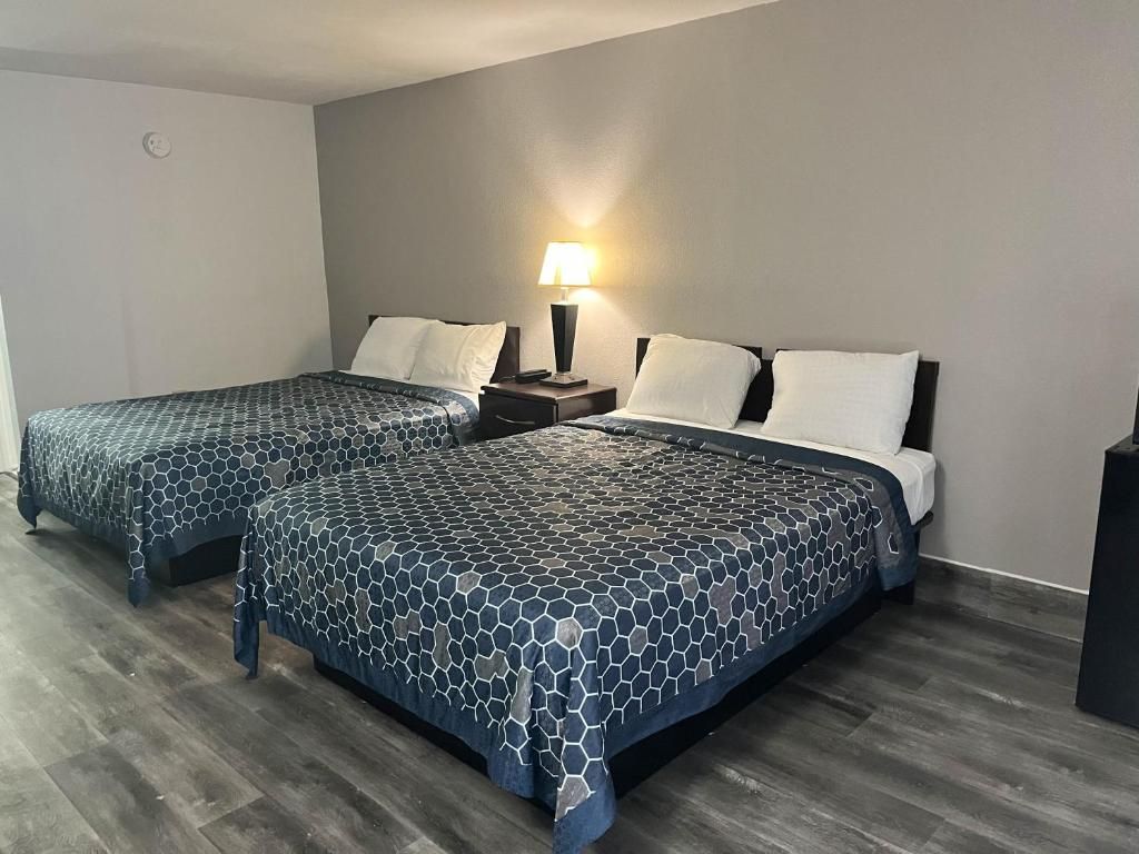 A hotel room with two beds, a nightstand with a lamp, and a wooden floor.