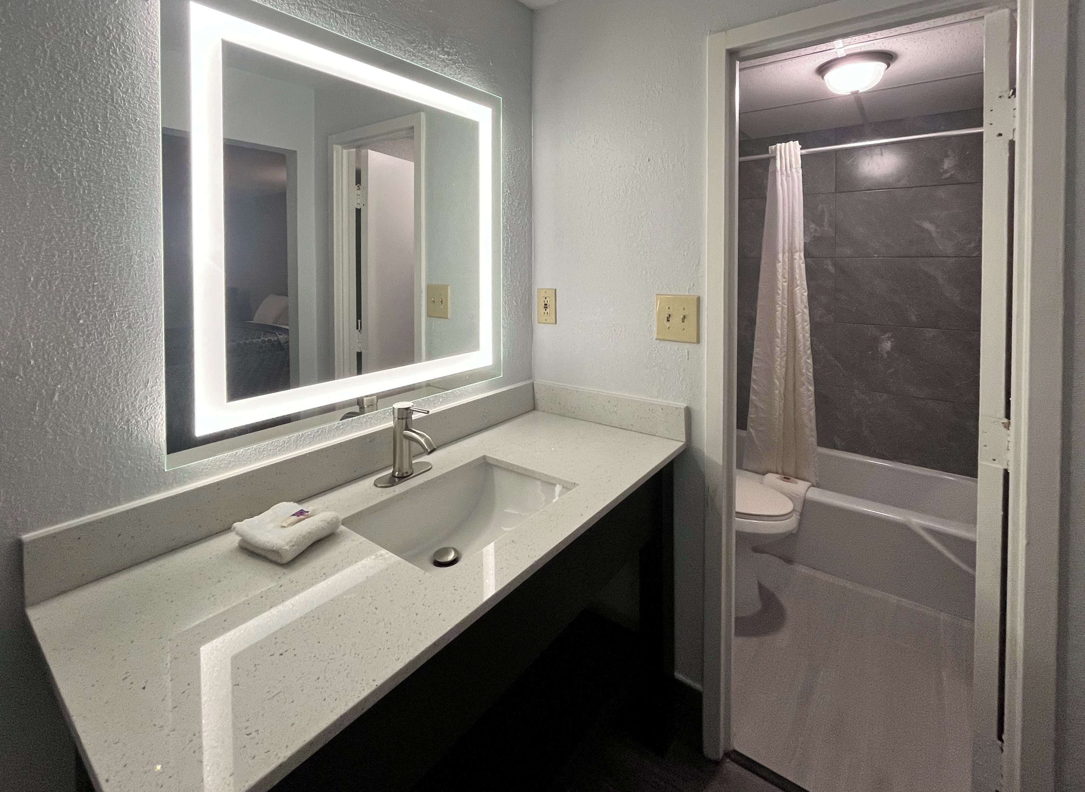 Un baño con lavamanos blanco, un espejo con luz y una ducha con cortina.