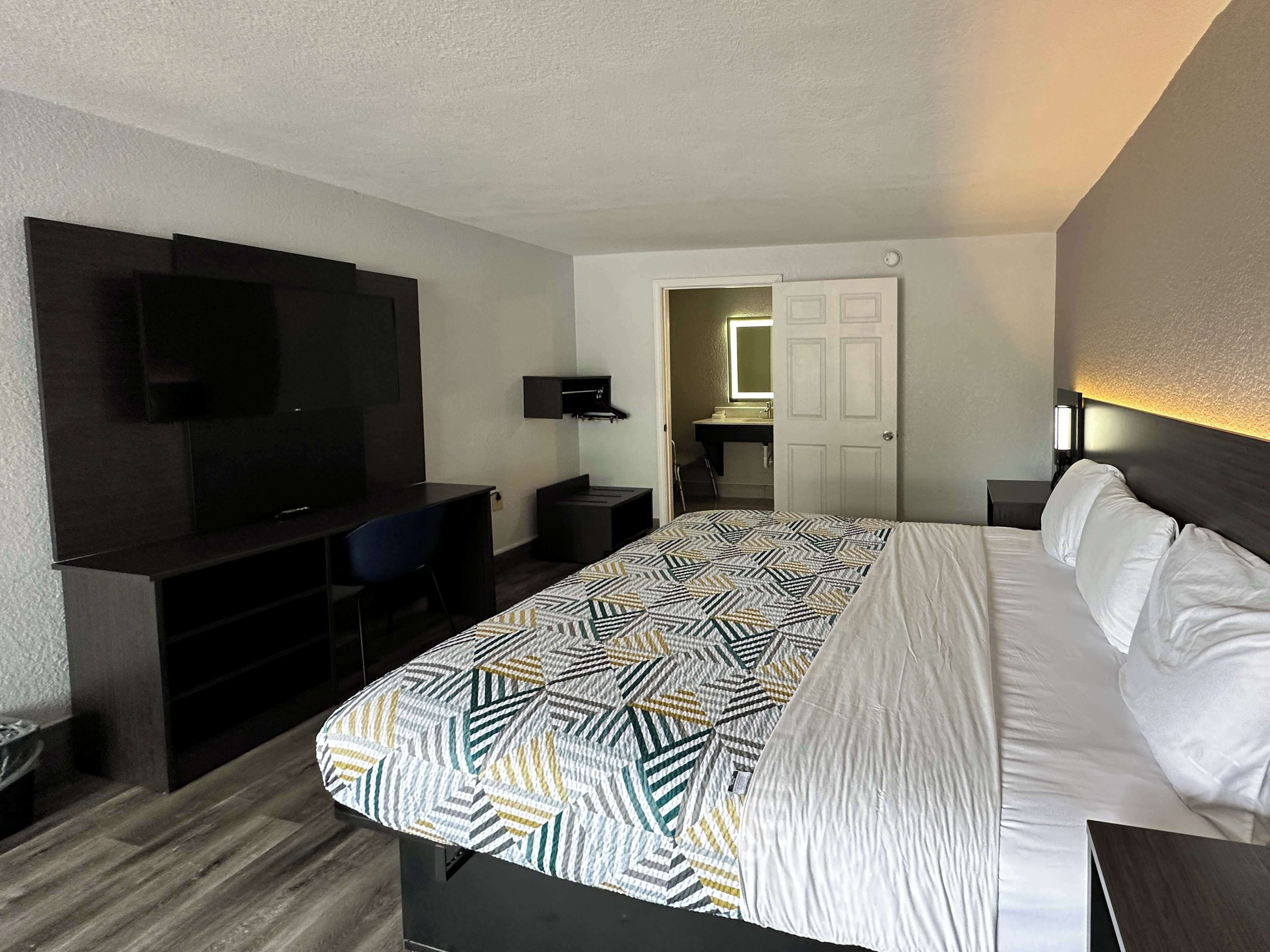 A hotel room with a bed, a desk, a TV, and a bathroom visible through an open door.