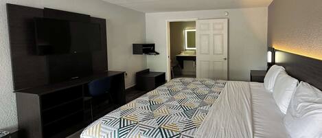 A hotel room with a bed, a desk, a TV, and a bathroom visible through an open door.