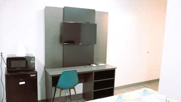 A compact hotel room with a bed, a desk with a chair, a microwave, and a television mounted on the wall.