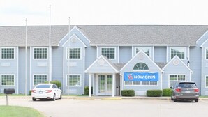 Un grand immeuble à étages, sur lequel on peut voir une grande enseigne indiquant « OUVERT MAINTENANT », un parking et quelques voitures garées devant.