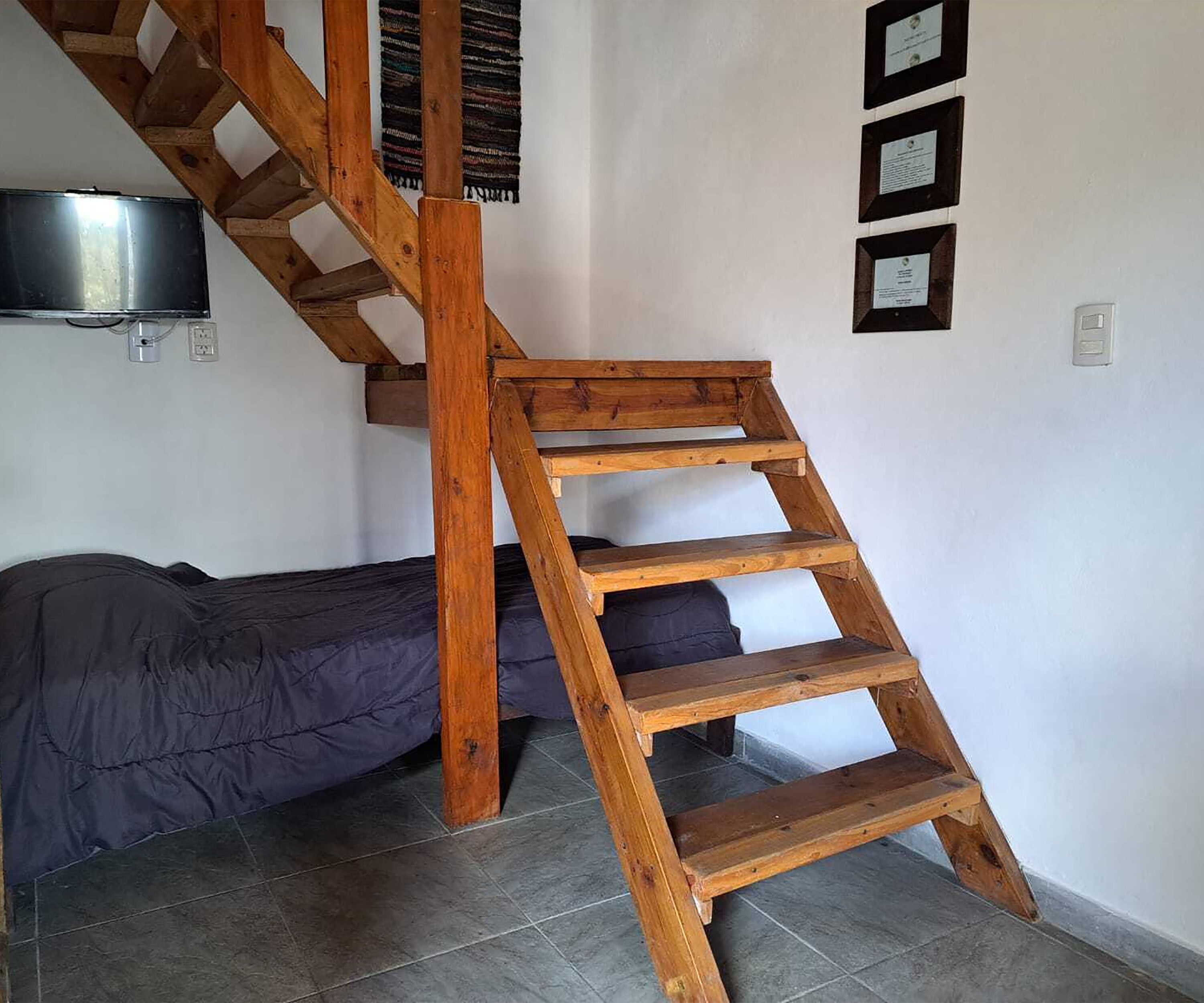 A wooden staircase in a room with a bed and a mounted television.