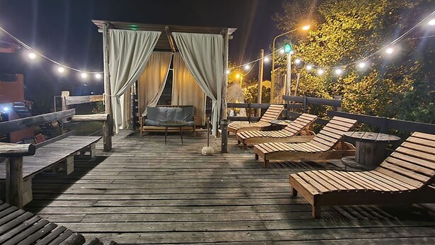 A wooden deck with lounge chairs and a covered seating area at night.