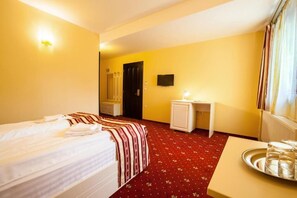 A hotel room with a bed, bedside table, and a small desk with a lamp. - Hotel Extravagance (Sighisoara)