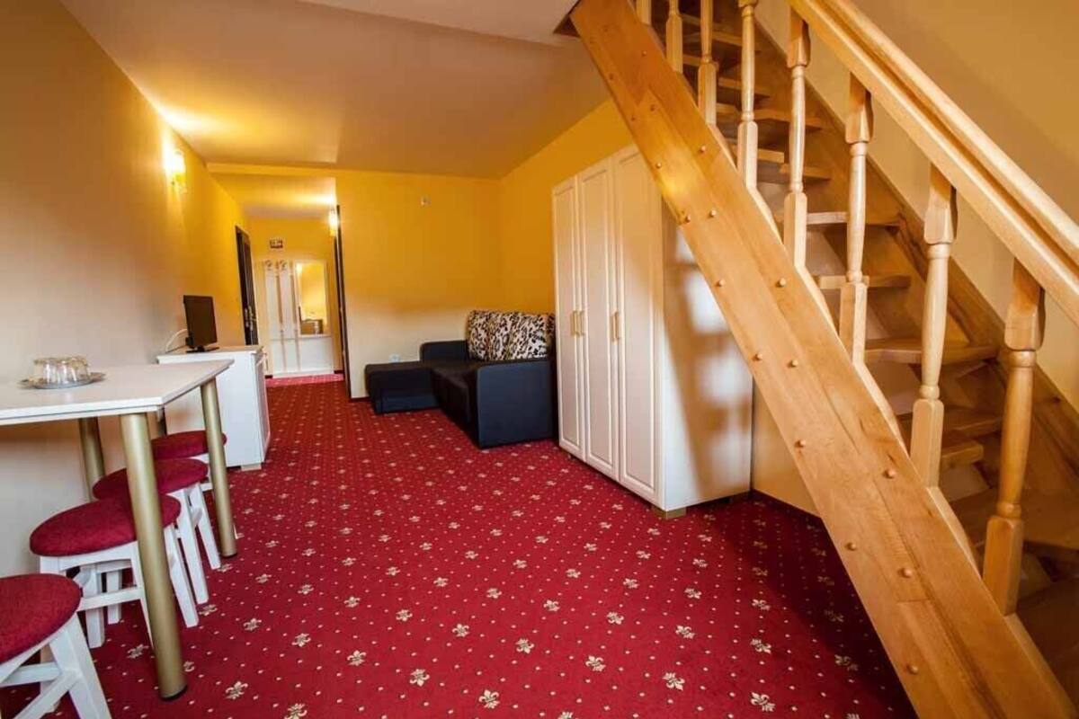 A room with a red carpet, a wooden staircase, a white wardrobe, and a small seating area with a patterned cushion.