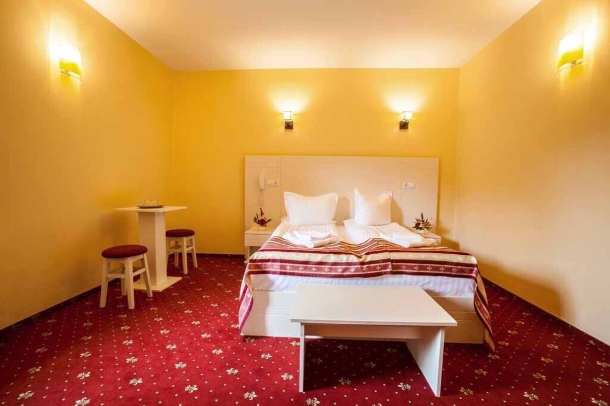 A hotel room with a bed, bedside tables, and a small desk with two chairs.