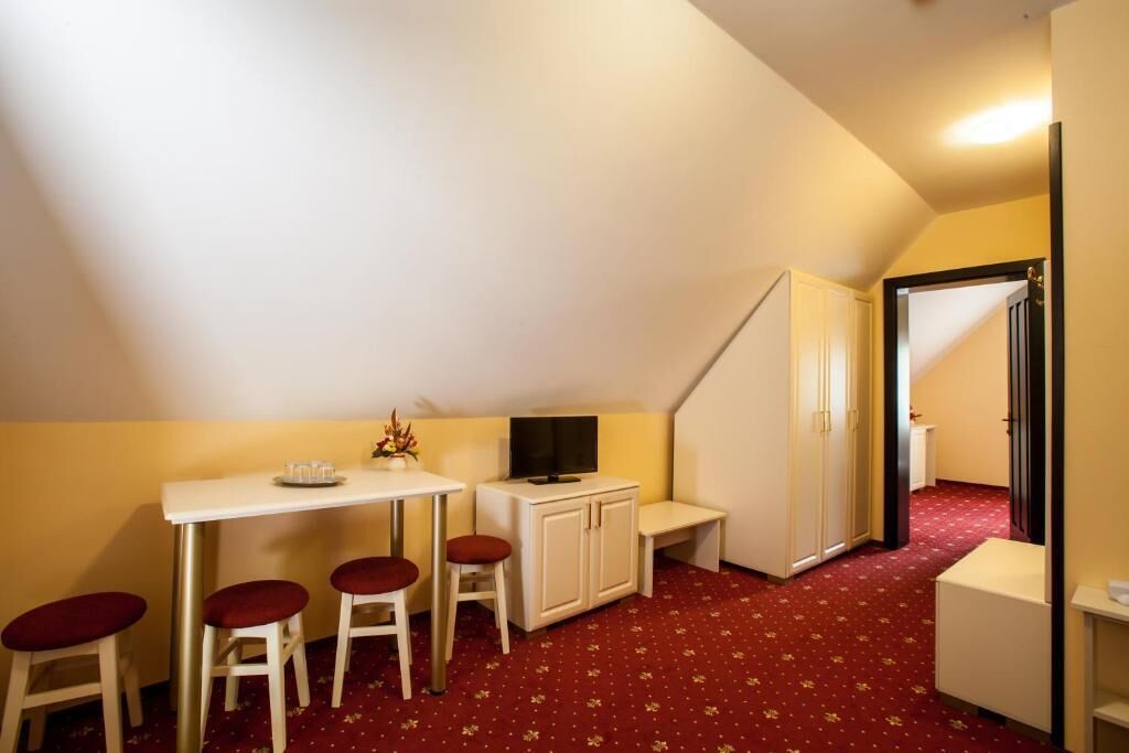 A small, cozy room with a white desk, two red cushioned chairs, a television, and a cabinet.