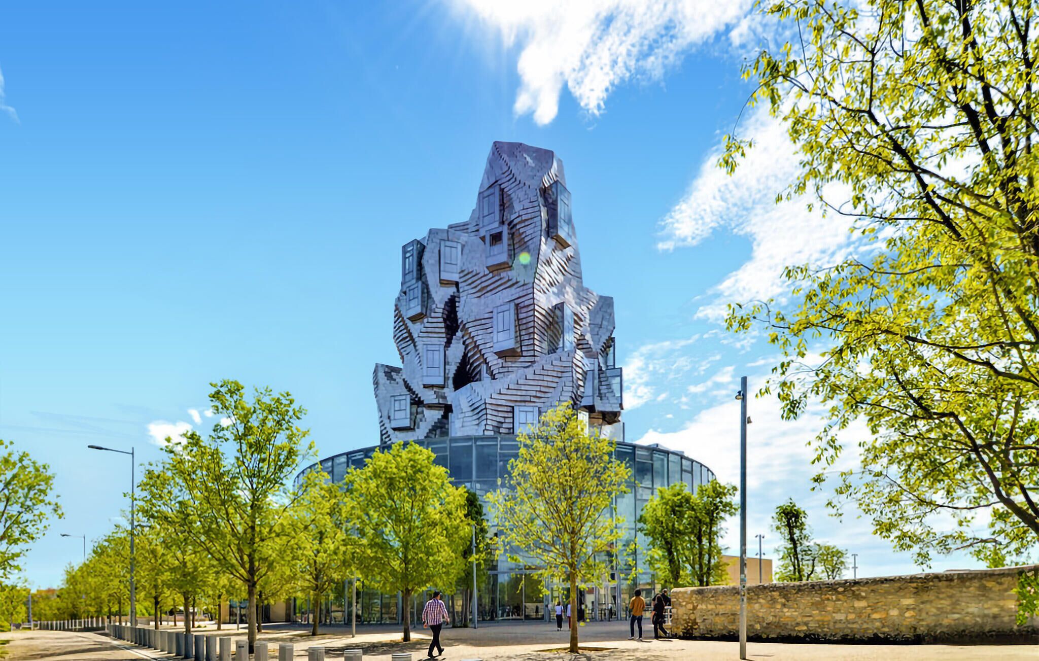 Ein modernes Gebäude mit einzigartigem, eckigem Design, umgeben von einer angelegten Grünfläche mit Bäumen und blauem Himmel.