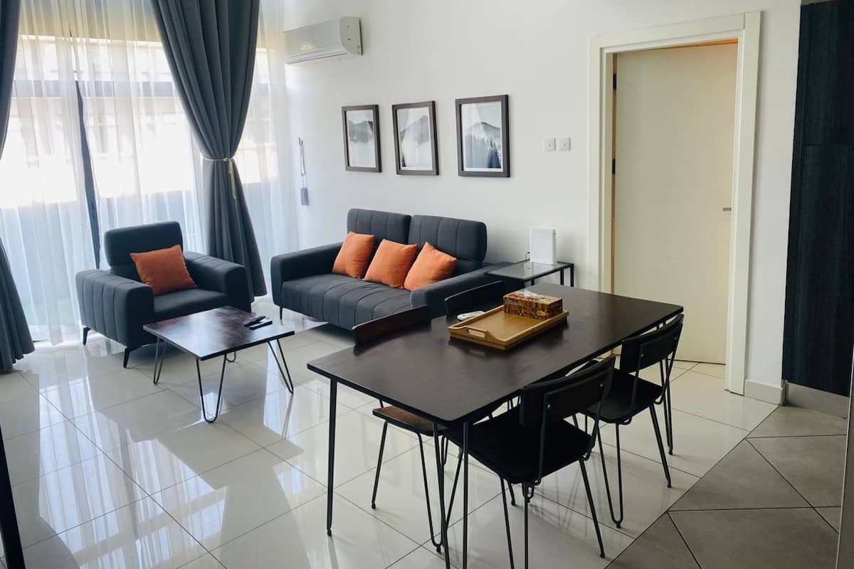 Una sala de estar moderna con un sofá, dos sillones, una mesa de centro y una mesa de comedor con sillas. Hay tres cuadros enmarcados en la pared, una puerta y un equipo de aire acondicionado.
