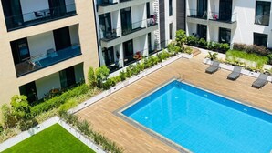 A modern building with multiple balconies, a swimming pool, and a well-maintained lawn.