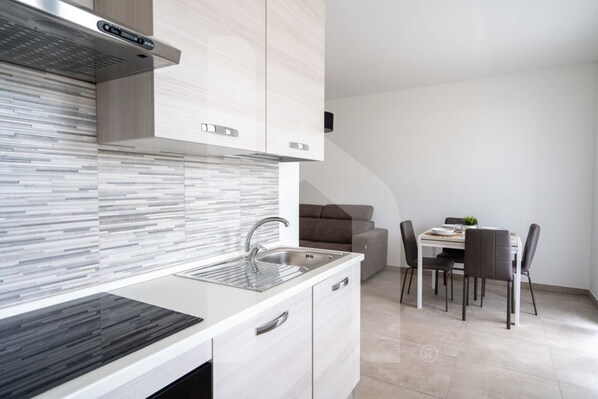 Una cucina moderna con lavello in acciaio inossidabile, mobili bianchi e schienale rivestito di piastrelle.