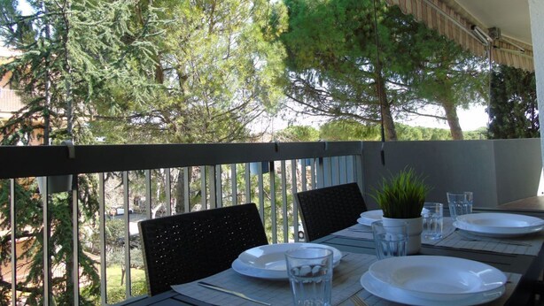 An outdoor dining area with a table set for two, surrounded by chairs, a small potted plant, and clear glasses.