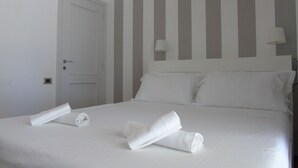 A neatly made bed with white linens and pillows, a closed door, and striped wall panels.