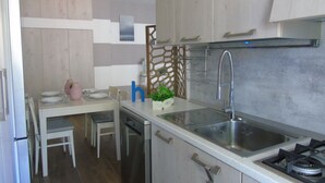 A modern kitchen with a white countertop, stainless steel sink, and a gas stove. There is a dining area with a white table and chairs.