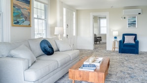 A living room with a light grey sofa, a wooden coffee table, and a blue armchair. There are two doors leading to other rooms, and a painting is on the wall. - Gorgeous Oceanfront Suite! (Hampton)