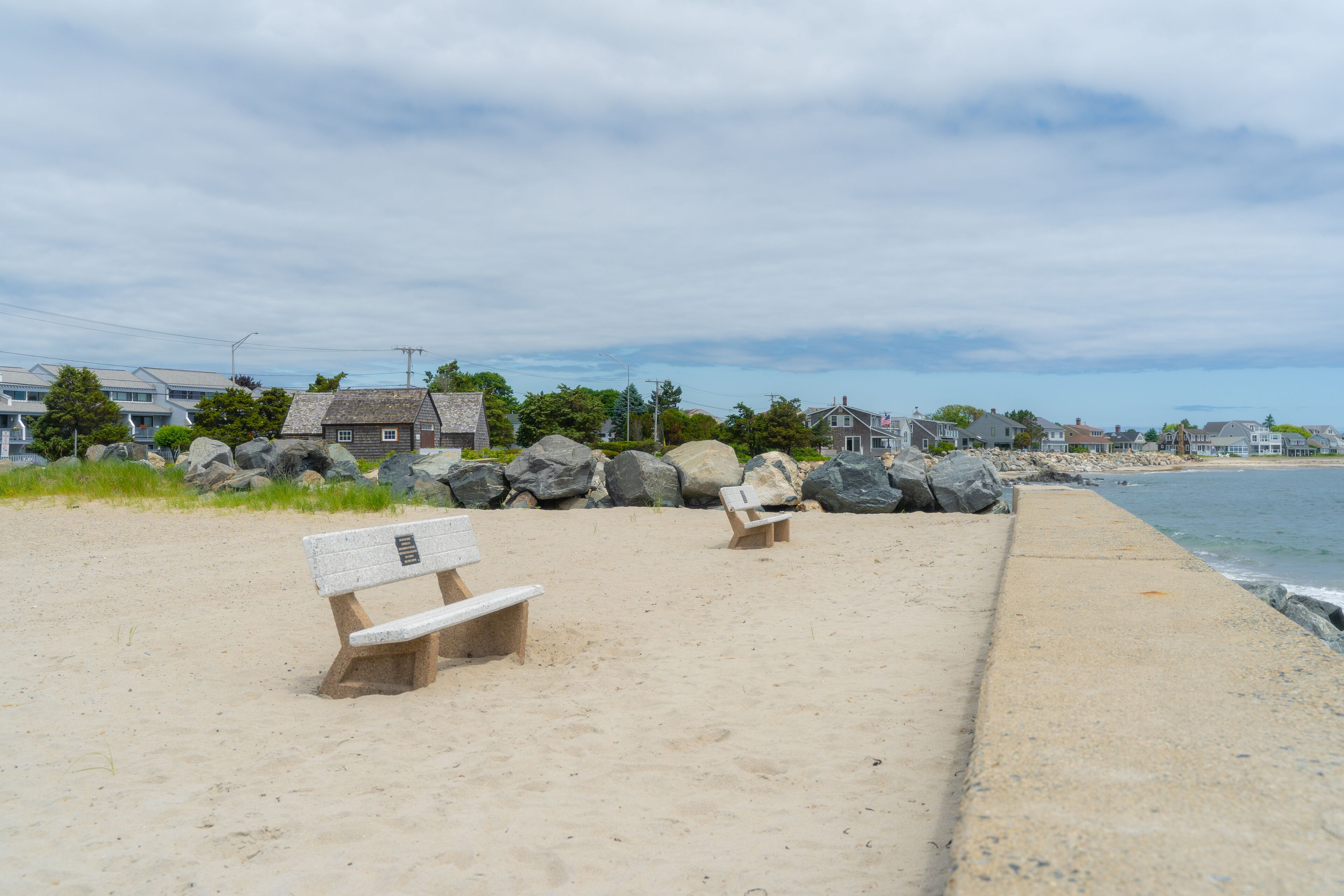 Une plage de sable avec deux bancs en bois et une promenade en béton.