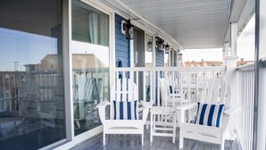 Un portico riparato con poltrone Adirondack bianche e cuscini a righe blu, ampie finestre e vista su edifici sullo sfondo.