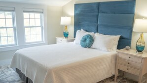 A neatly made bed with a white quilted bedspread, a blue headboard, and two bedside lamps. - Oceanside queen room with lounge area! (Hampton)