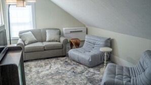 A cozy loft bedroom with a gray sofa, a small wooden stool, and a white table. - Oceanside queen room with lounge area! (Hampton)