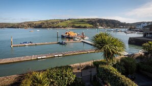 A coastal harbor with boats docked at a wooden pier, surrounded by greenery and hills in the background. - Lifeboat Cottage -  a cottage that sleeps 2 guests  in 1 bedroom (Salcombe)