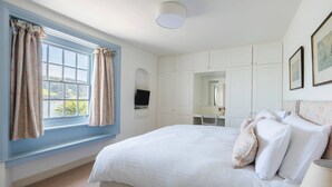 A bedroom with a large bed, a desk, and a wardrobe. - Lifeboat Cottage -  a cottage that sleeps 2 guests  in 1 bedroom (Salcombe)