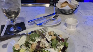 A dining table with a salad, a glass of water, bread, and condiments. - Beachfront, clean, quiet, luxury condo on 3 rd fl amazing view! Walk to Tootsies (Panama City Beach)