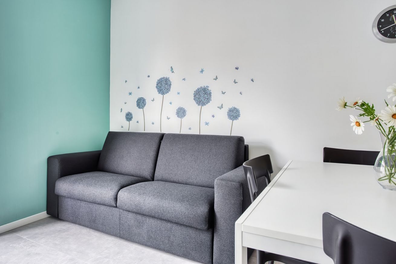 Een moderne woonkamer met een grijze bank, een witte eettafel en een wand met een decoratie geïnspireerd door de natuur.