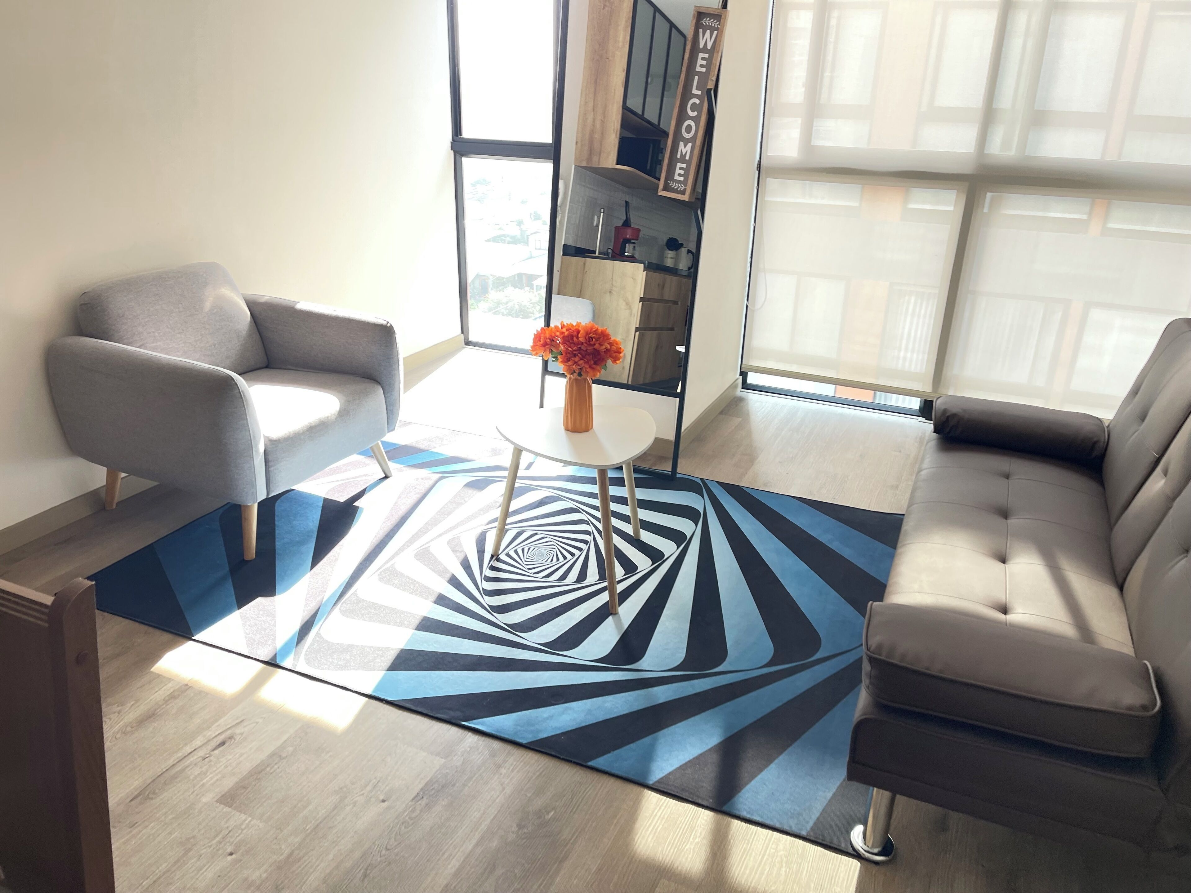 A modern living room with a sofa, armchair, coffee table, and a patterned rug.