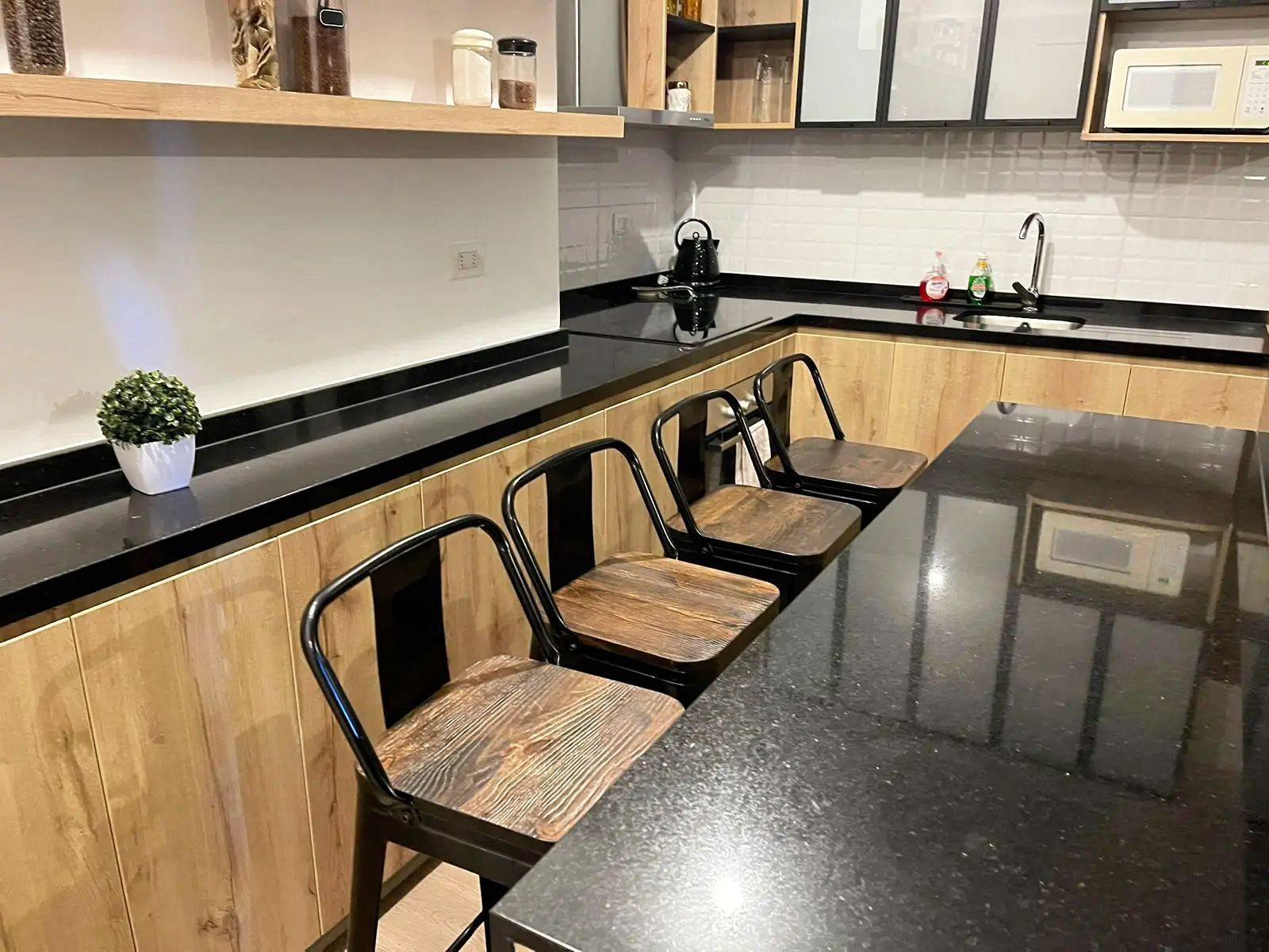 Une cuisine moderne avec des meubles en bois, un plan de travail noir et trois chaises noires dotées d’assises en bois.