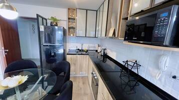 A modern kitchen with a refrigerator, microwave, and a dining area with a glass table and chairs.
