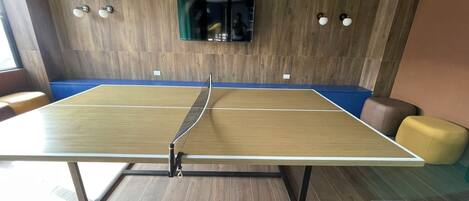 A ping pong table in a room with wooden flooring and a blue cushioned bench.