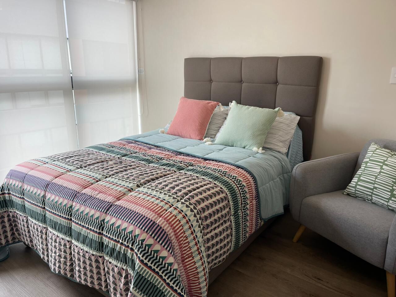 A bedroom with a bed, a grey sofa, and a patterned bedspread.