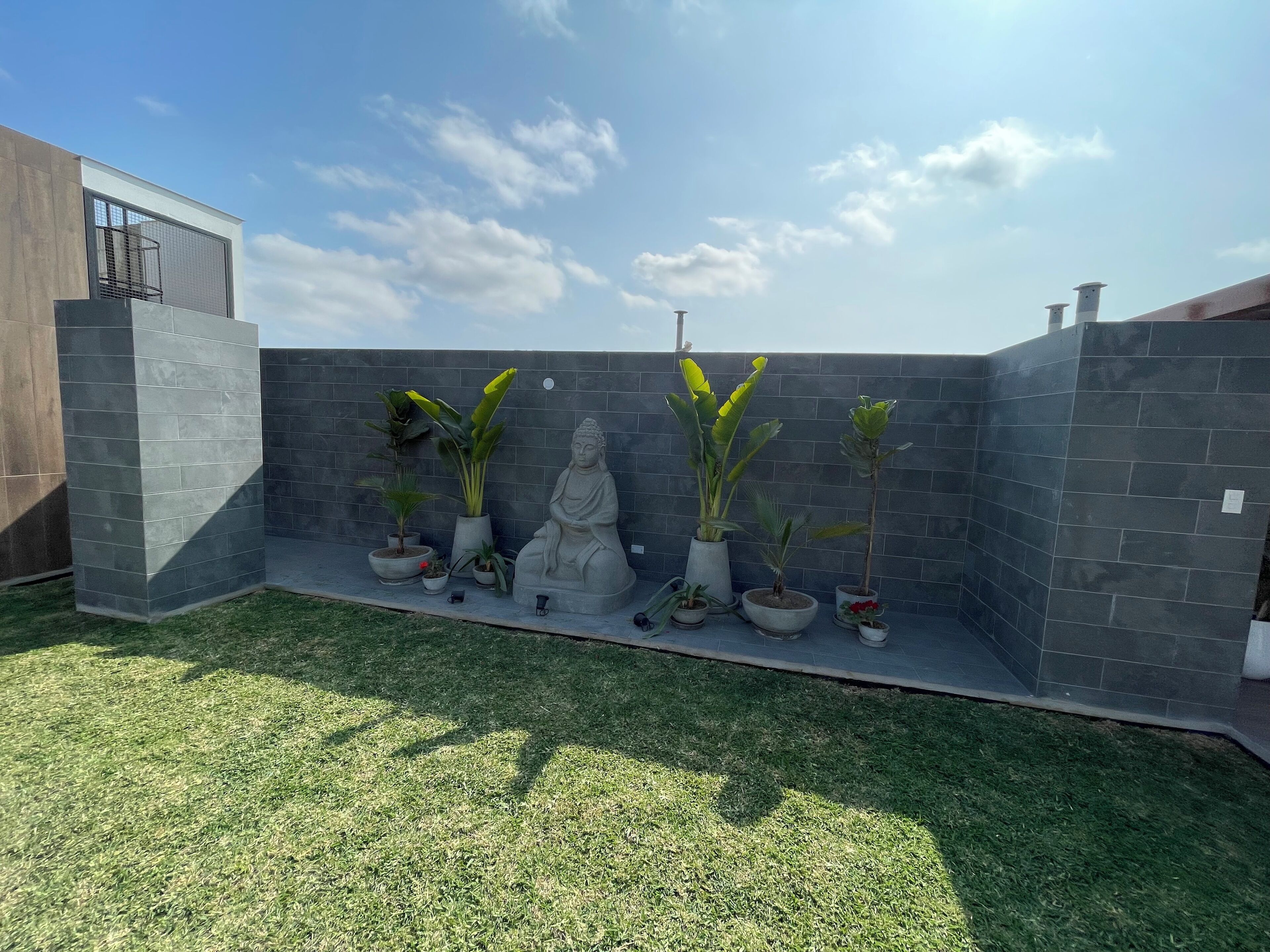 Uma área externa moderna com uma parede de pedra, plantas em vasos e uma estátua de Buda.
