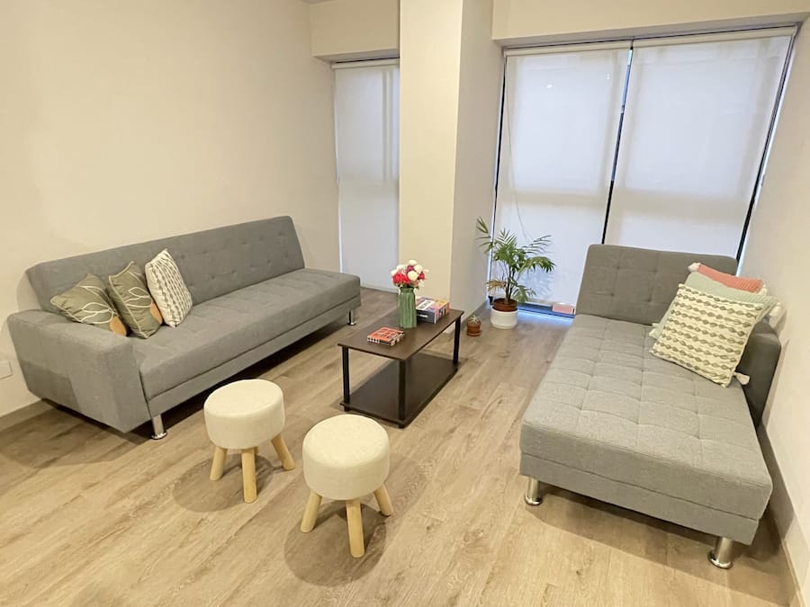 Una sala de estar moderna con dos sofás grises, una mesita de centro y dos taburetes de madera.